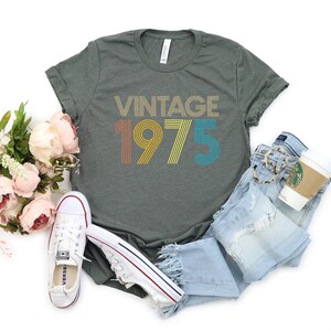 May include: A green t-shirt with the text "Vintage 1975" in rainbow colors. The text is in a retro font style.