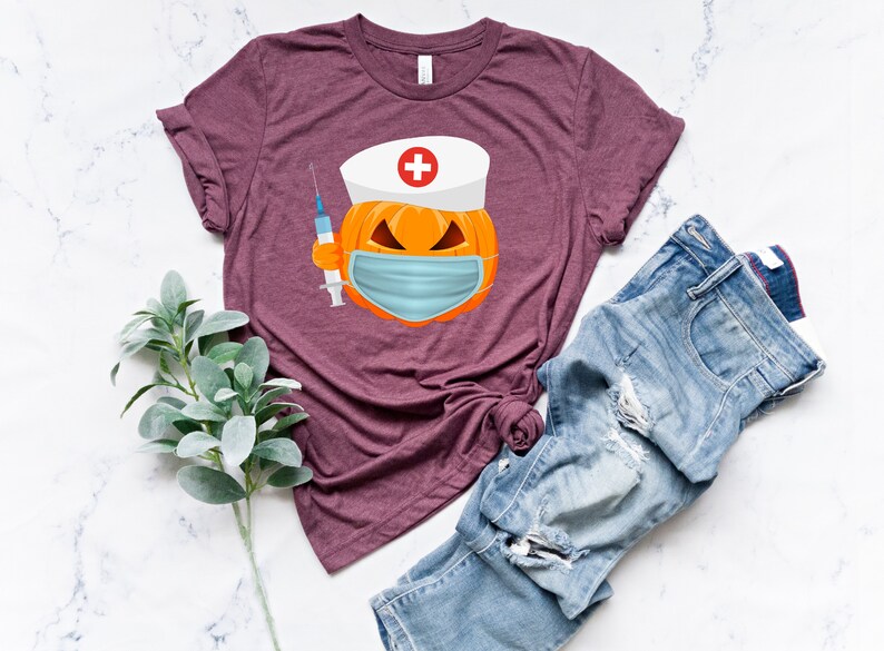 May include: A maroon t-shirt with a graphic of a pumpkin wearing a nurse's hat and a face mask. The pumpkin is holding a syringe.