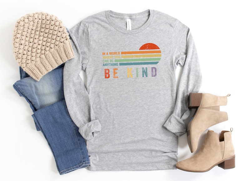 May include: A grey long-sleeved t-shirt with a rainbow stripe design and the text "In a world where you can be anything be kind".