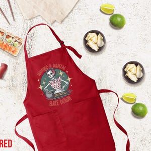 May include: Red kitchen apron with a skeleton baking and the text "Having a mental bake down".