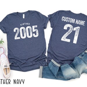 a pair of blue t-shirts with the text "VINTAGE 2005" and "CUSTOM NAME 21" printed on them, along with a pair of jeans and sneakers.