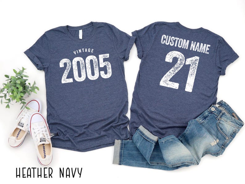 a pair of blue t-shirts with the text "VINTAGE 2005" and "CUSTOM NAME 21" printed on them, along with a pair of jeans and sneakers.