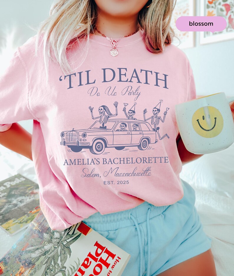 A woman wearing a pink t-shirt with a graphic design and holding a coffee mug with a smiley face.