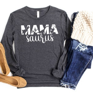 May include: A dark grey long-sleeved shirt with the text "Mama saurus" in white. The text is surrounded by a silhouette of dinosaurs.