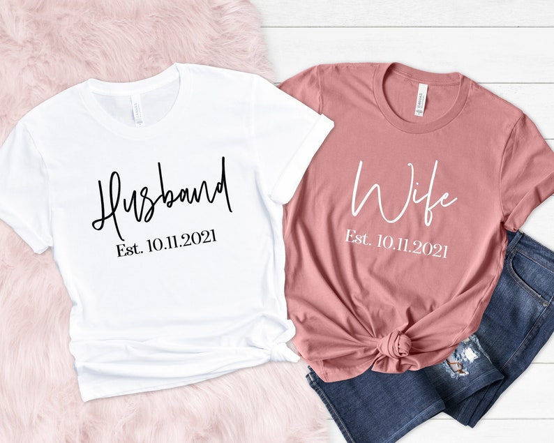 Puede incluir: Dos camisetas, una blanca y otra rosa, con las palabras "Husband Est. 10.11.2021" y "Wife Est. 10.11.2021" impresas en ellas.