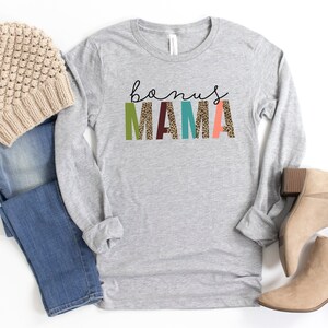 May include: Gray long-sleeve shirt with the text "bonus MAMA" in colorful letters with a leopard print pattern.