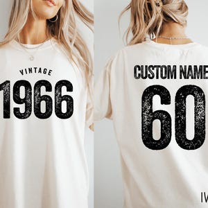 A white t-shirt with the text "VINTAGE 1966" printed on it, along with the number "60" below it. The t-shirt also has the text "CUSTOM NAME" printed on the back.