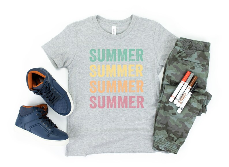 Puede incluir: Una camiseta gris con la palabra "SUMMER" repetida cuatro veces en diferentes colores. La camiseta se combina con pantalones de camuflaje, zapatillas azules de ca&ntilde;a alta y un juego de rotuladores de colores.