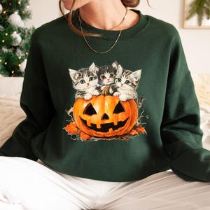 a woman sitting on a bed wearing a green sweater with kittens on it