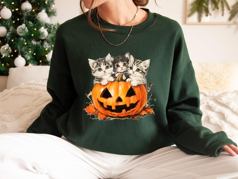 a woman sitting on a bed wearing a green sweater with kittens on it