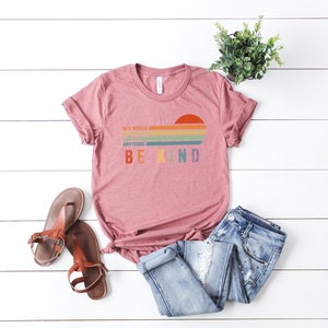 May include: A pink t-shirt with a rainbow sunset graphic and the text "In a world where you can be anything, be kind".