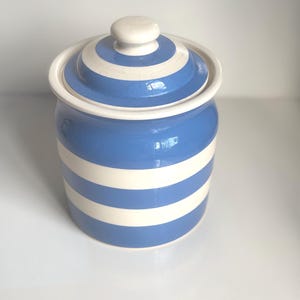 May include: A ceramic jar with a lid, featuring horizontal stripes in blue and white. The jar has a rounded shape with a matching lid and a small, round knob. The design is simple and classic, suitable for kitchen storage.