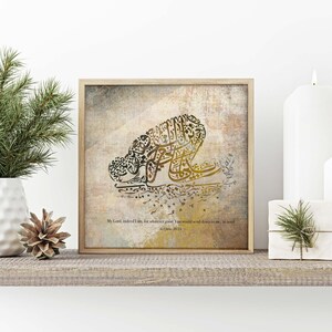May include: A framed print featuring Arabic calligraphy in shades of gold and brown, depicting a figure in prayer. The artwork is set against a textured background and includes a quote. The frame is a light wood color.