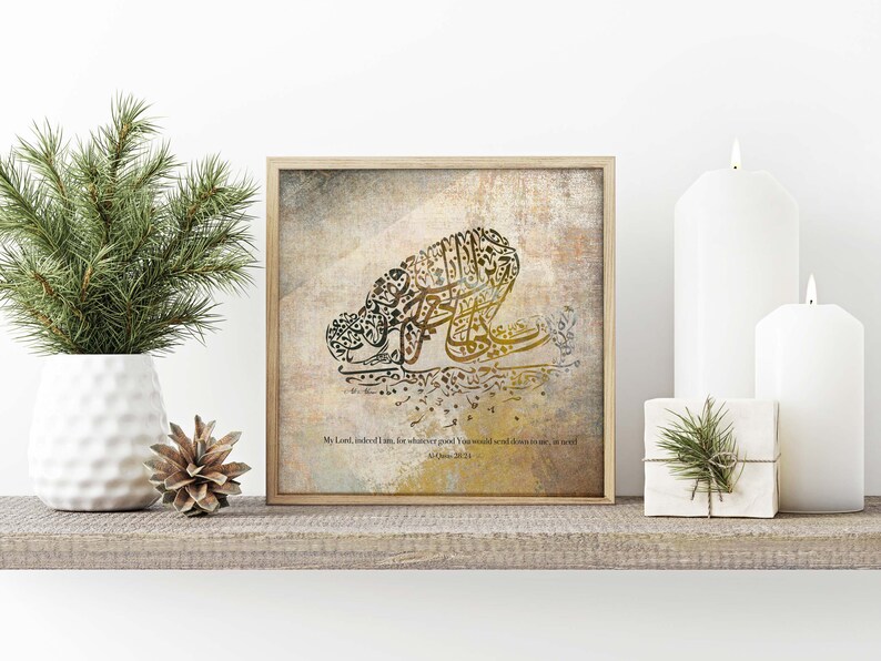 May include: A framed print featuring Arabic calligraphy in shades of gold and brown, depicting a figure in prayer. The artwork is set against a textured background and includes a quote. The frame is a light wood color.