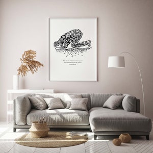 May include: A framed black and white art print featuring Arabic calligraphy in the shape of a person in prayer. The print includes English text from the Quran. The artwork is displayed in a modern living room setting.