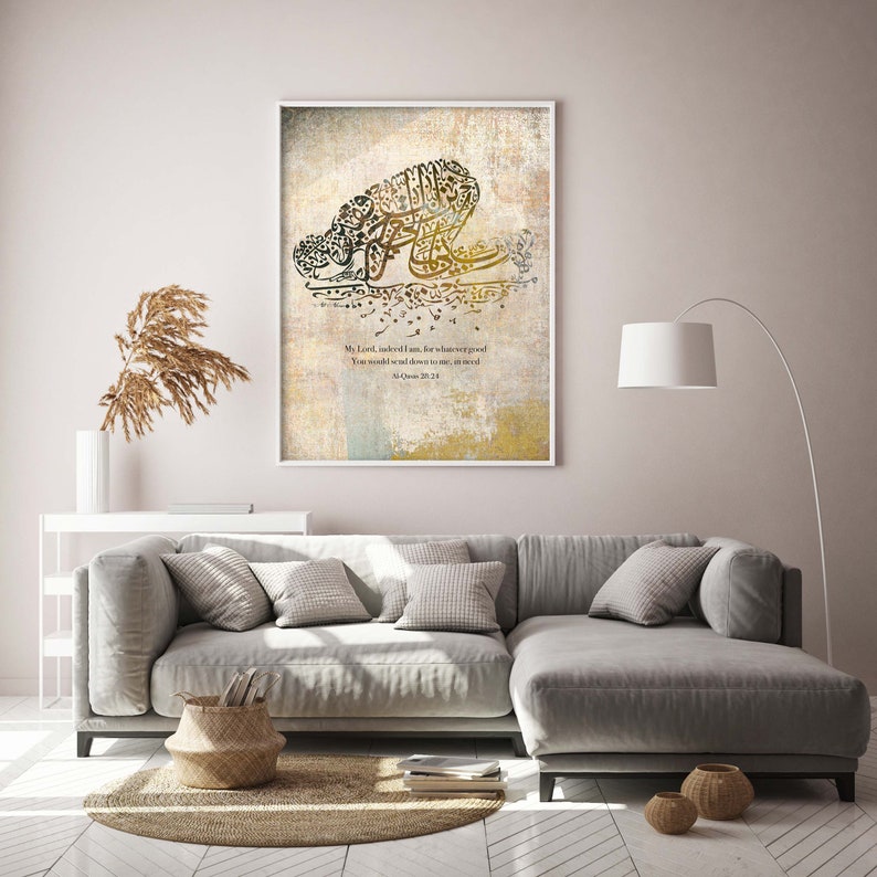 May include: Framed art print featuring Arabic calligraphy in shades of gold and black on a textured background. The artwork includes a prayer and is displayed in a white frame. The print is displayed in a living room setting.