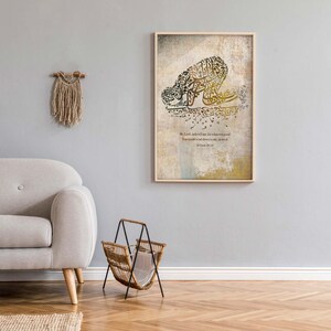 May include: A framed artwork featuring Arabic calligraphy in shades of gold and brown, depicting a figure in prayer. The artwork is displayed on a light gray wall, alongside a beige sofa, a woven magazine rack, and a decorative wall hanging.