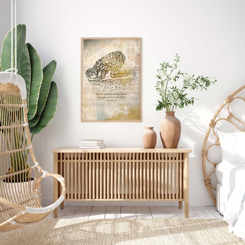 May include: A framed print featuring Arabic calligraphy in black and gold, depicting a figure in prayer. The artwork is set against a textured, neutral-toned background with a quote in English. The frame is a light wood color.