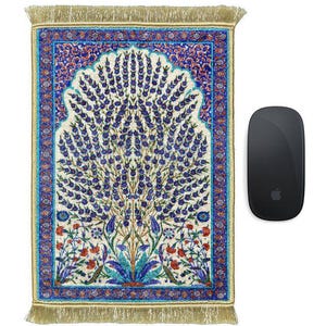 Può includere: Un tappeto da preghiera ornato con un disegno centrale ad albero in blu e bianco, incorniciato da un bordo blu con accenti floreali rossi. Un mouse per computer nero è a destra.