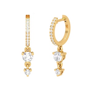 May include: Gold hoop earrings with a dangling charm featuring three round clear stones. The hoop is accented with a row of small clear stones.
