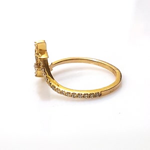 K&ouml;nnte beinhalten: Ein goldener Ring mit einem gebogenen Band und einem kleinen Cluster aus klaren Steinen an der Seite. Das Band ist mit kleinen klaren Steinen besetzt.