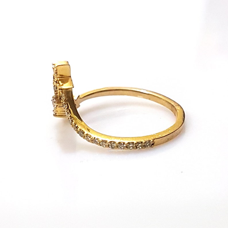 K&ouml;nnte beinhalten: Ein goldener Ring mit einem gebogenen Band und einem kleinen Cluster aus klaren Steinen an der Seite. Das Band ist mit kleinen klaren Steinen besetzt.