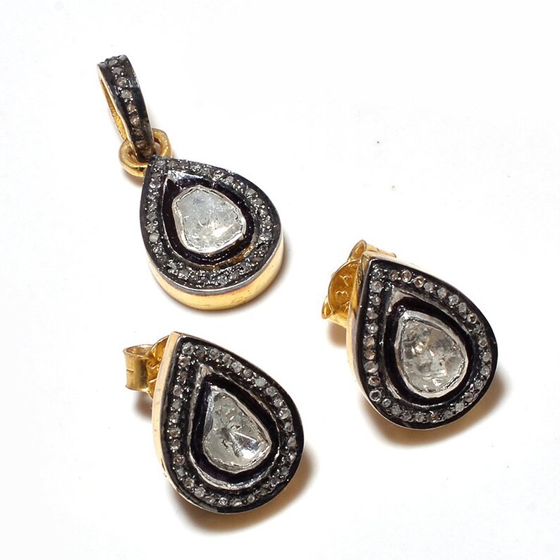 May include: A set of gold and silver teardrop-shaped earrings with a diamond-shaped stone in the center. The earrings are surrounded by a black border and small diamonds.