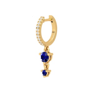May include: Gold hoop earring with a dangling charm featuring two blue sapphires.