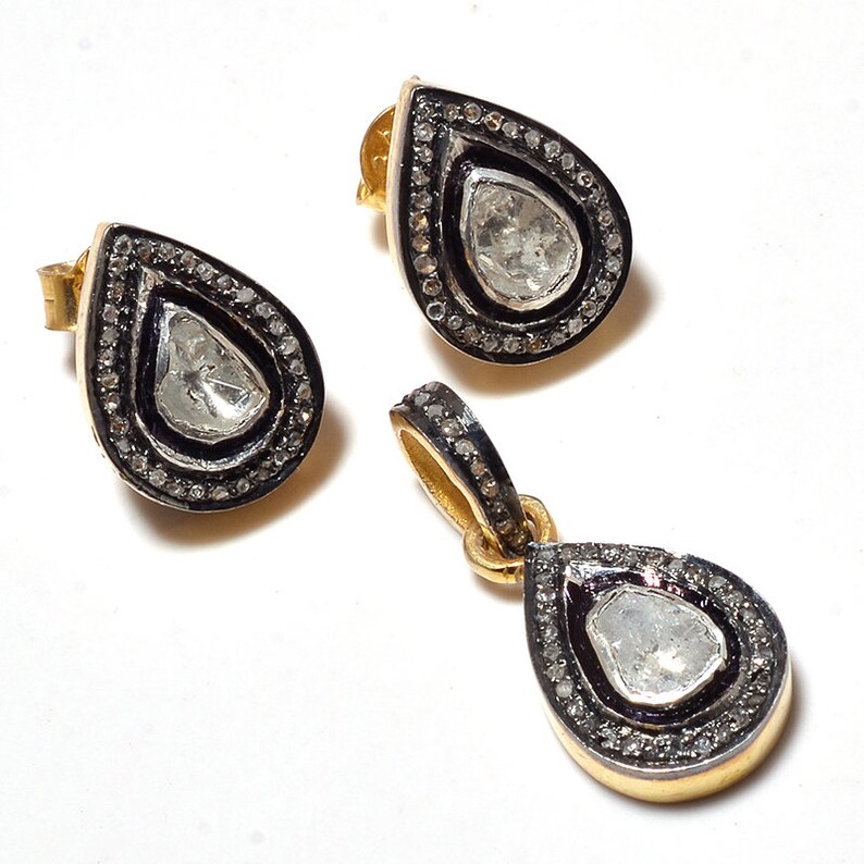 May include: A set of silver earrings and a pendant featuring a teardrop-shaped diamond with a black border and a smaller diamond halo.