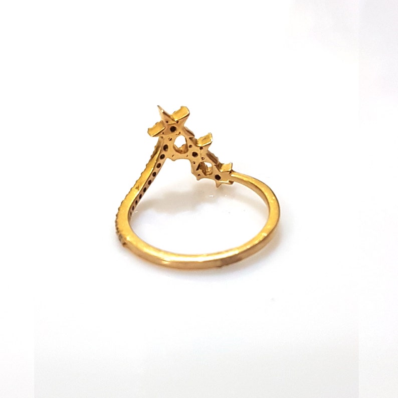 K&ouml;nnte beinhalten: Ein goldener Ring mit einem zarten, sternf&ouml;rmigen Design. Der Ring ist mit kleinen, funkelnden Steinen besetzt.