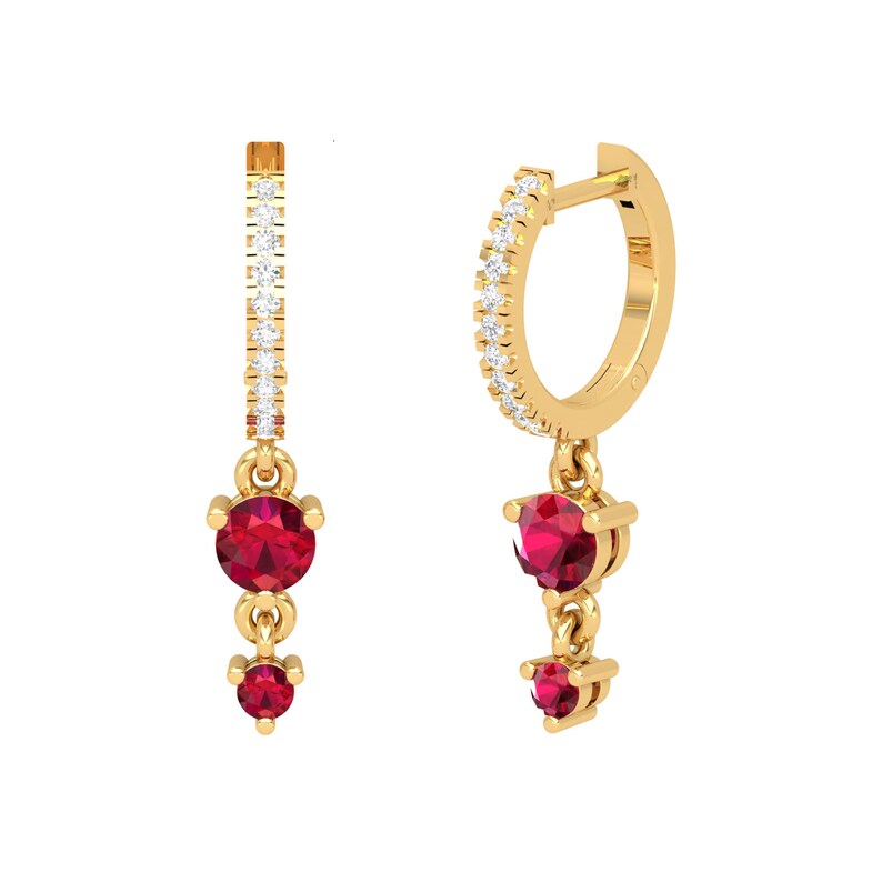 May include: Gold hoop earrings with a dangling charm featuring two red gemstones. The hoop is accented with a row of small clear gemstones.
