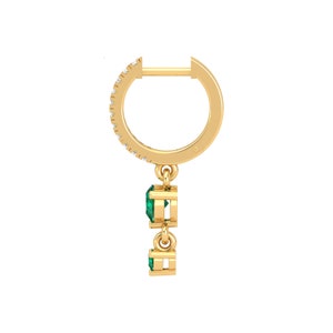 May include: Gold hoop earrings with a dangling emerald green gemstone drop. The hoop is accented with small clear stones.