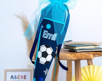 Peut inclure: Un cône scolaire bleu et blanc avec un motif de ballon de football et le nom "Emil" dessus. Le cône est décoré d'étoiles et de points bleus et argentés. Il est attaché avec un ruban bleu et de la tulle.
