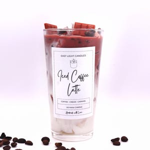 Peut inclure: Un bocal en verre pour bougie avec un motif de latte glacé au café rouge et blanc. La bougie est en cire de soja et a un parfum de café, crème et caramel. L'étiquette indique "East Light Candles" et "Iced Coffee Latte".