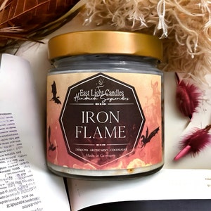 Puede incluir: Un tarro de vela negro y dorado con una etiqueta que dice "East Light Candles Handmade Soycandles IRON FLAME DRAGONS ARCTIC MINT COCOSUGAR Made in Germany".