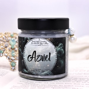 Może przedstawiać: Szklany słoik z szarym woskiem i czarną pokrywką. Na etykiecie widnieje napis "East Light Candles Handmade Soy Candles" oraz "Azriel" na tle galaktyki.  Zapach świecy to bursztyn, bursztyn i magnolia.