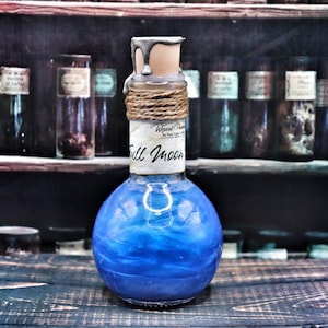 Peut inclure: Une bouteille en verre bleu avec un bouchon en liège et argent, enveloppé de ficelle. La bouteille est remplie d'un liquide bleu chatoyant et porte une étiquette qui indique "Wizard Potion by Raven Light Candles Full Moon".