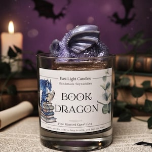 Pode incluir: Um frasco de vela de vidro transparente com uma figura de dragão roxo no topo. O rótulo diz "BOOK DRAGON" com o texto "East Light Candles" e "Fire Roasted Chestnuts". Uma vela acesa e silhuetas de morcegos no fundo.
