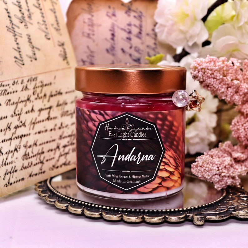 Pu&ograve; includere: Una piccola candela di vetro in un barattolo con un coperchio di rame. La candela &egrave; di colore rosso scuro e ha un'etichetta che recita "Handmade Soycandles East Light Candles Andarna Fourth Wing Dragon & Hencus Nectar Made in Germany".
