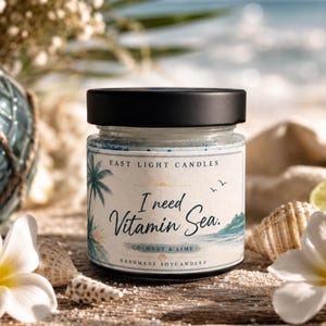 Könnte beinhalten: Ein Glas-Kerzenglas mit schwarzem Deckel, beschriftet mit "I need Vitamin Sea" mit einer Palme und einer Ozeanszene. Die Kerze ist nach "Kokosnuss & Limette" duftend und ist von Muscheln und Blumen umgeben.