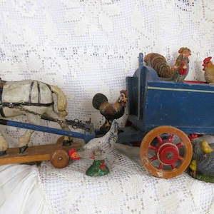 May include: A vintage wooden toy set featuring a white horse pulling a cart with a blue body and red wheels. The cart is filled with rooster and hen figurines. The set is painted in various colours.