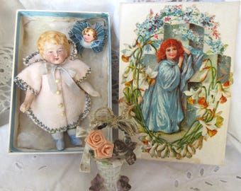 Puede incluir: Dos cajas vintage con muñecas de porcelana en su interior. La muñeca de la izquierda lleva un vestido rosa con zapatos azules y un sombrero azul y blanco. La muñeca de la derecha lleva un vestido azul y está de pie en un entorno floral.