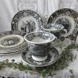 May include: A set of black and white teacups and saucers with intricate floral designs. The cups and saucers feature black and white illustrations of people and landscapes.