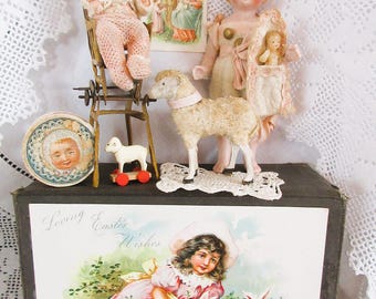 Può includere: Una collezione di oggetti vintage a tema pasquale, tra cui bambole, una statuina di agnello e una cartolina con la scritta "Loving Easter Wishes". Le bambole indossano abiti rosa e color crema. La cartolina presenta una ragazza con conigli.