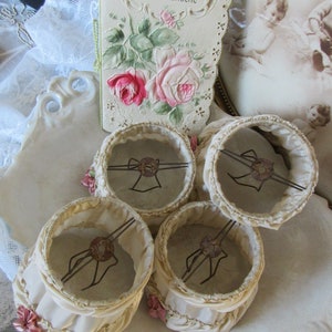 May include: Four vintage lampshades with ruffled edges and delicate pink flowers. The lampshades are made of a cream-colored fabric and have a wire frame.