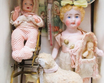 Puede incluir: Colección de muñecas y juguetes antiguos, que incluye una muñeca bebé con ropa rosa, una muñeca con un lazo amarillo, un cordero de juguete con un collar rosa y una pequeña muñeca bebé en un portabebés rosa. También hay una imagen religiosa vintage y una imagen redonda de un bebé.