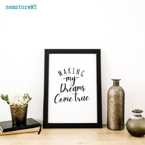 Op de afbeelding: Een zwarte fotolijst met een witte print en de zwarte tekst "MAKING my Dreams Come true". Links staat een gestructureerde, metallic bronzen vaas met witte bloemen op twee boeken. Rechts staan twee metallic bronzen vazen.