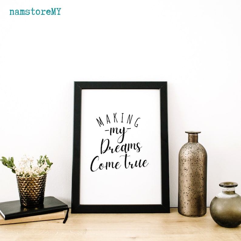 Op de afbeelding: Een zwarte fotolijst met een witte print en de zwarte tekst "MAKING my Dreams Come true". Links staat een gestructureerde, metallic bronzen vaas met witte bloemen op twee boeken. Rechts staan twee metallic bronzen vazen.