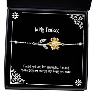 May include: A black gift box containing a white sunflower charm bracelet. The box has a white inscription that reads "To My Fiancee" and "I'm not getting less energetic, I'm just redirecting my energy into loving you more."
