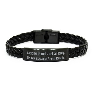 May include: Black leather bracelet with a black metal plate that reads "Cooking is not just a hobby. It's my escape from reality."